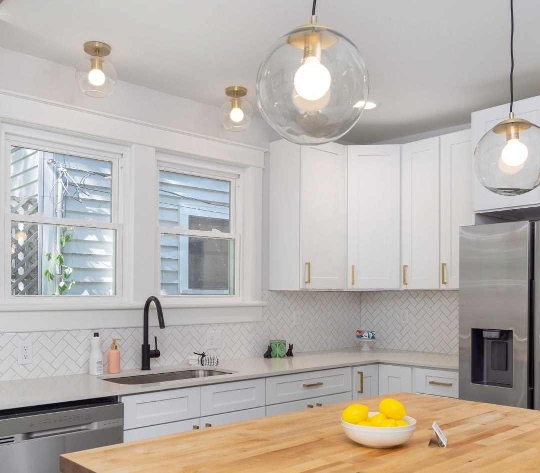 Kitchen after: white cabinets, glass pendants and a butcher-block island