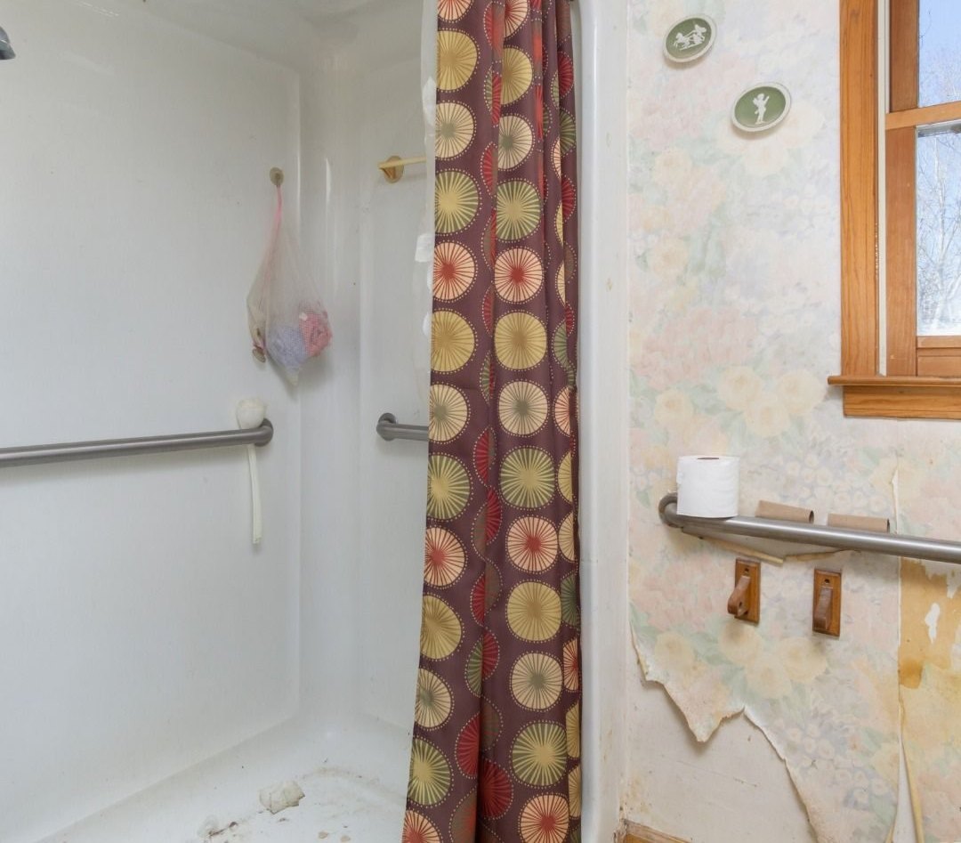 Shower before: plastic surround with grab bars and a patterned curtain