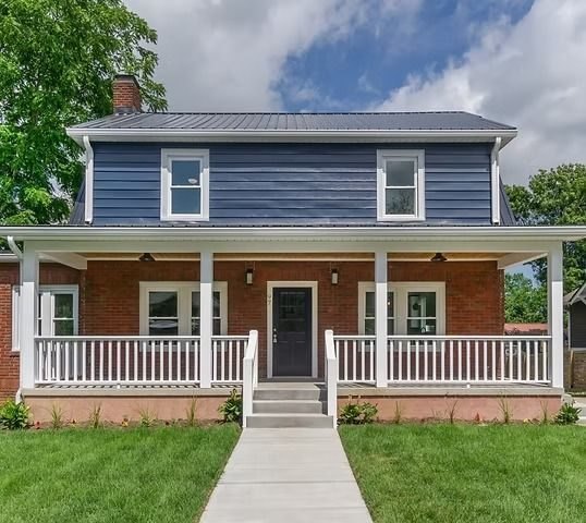 Two-story house after: navy siding above a brick porch with white railings