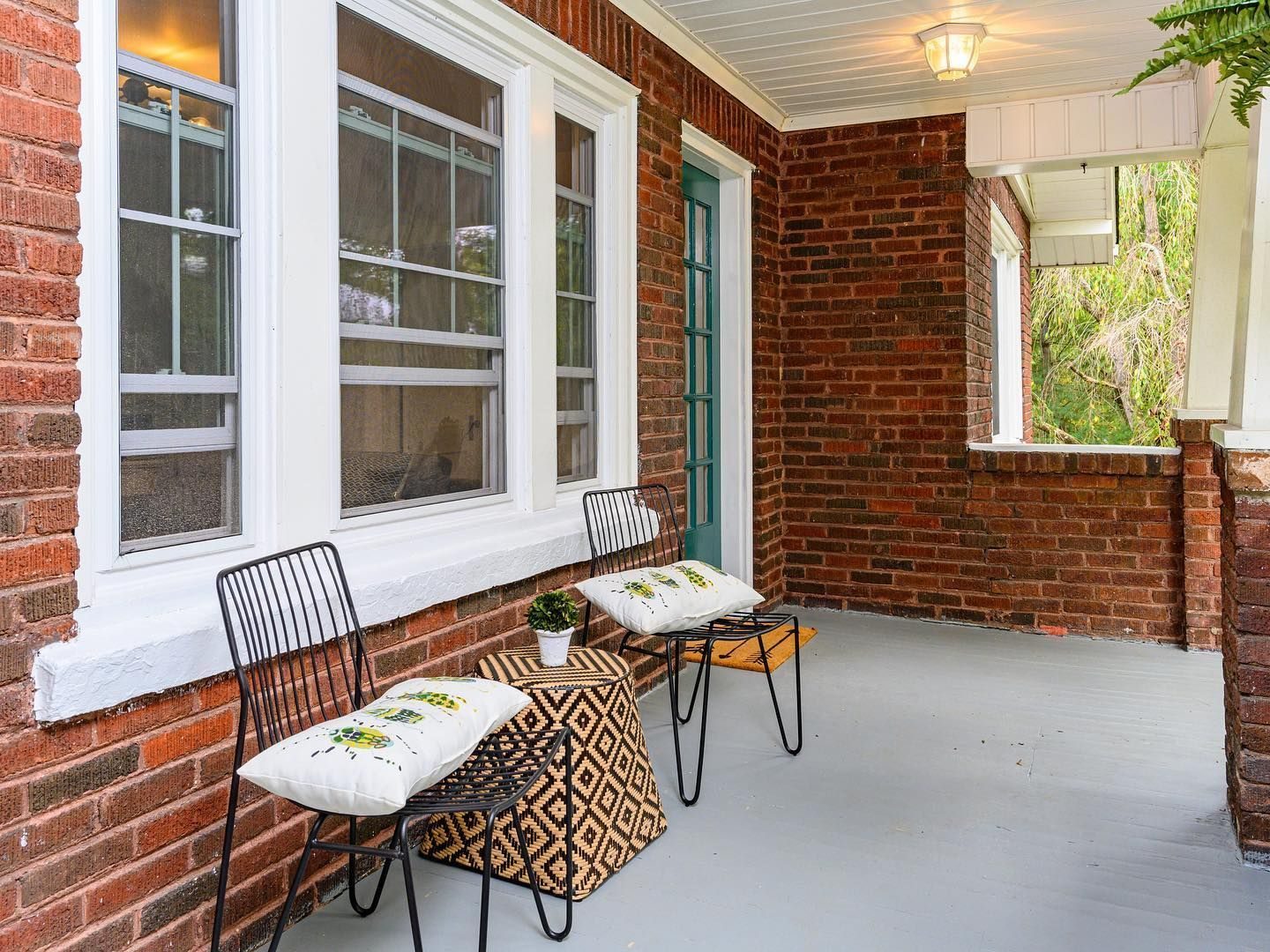 Brick porch with white trim, wire chairs and a ceiling light