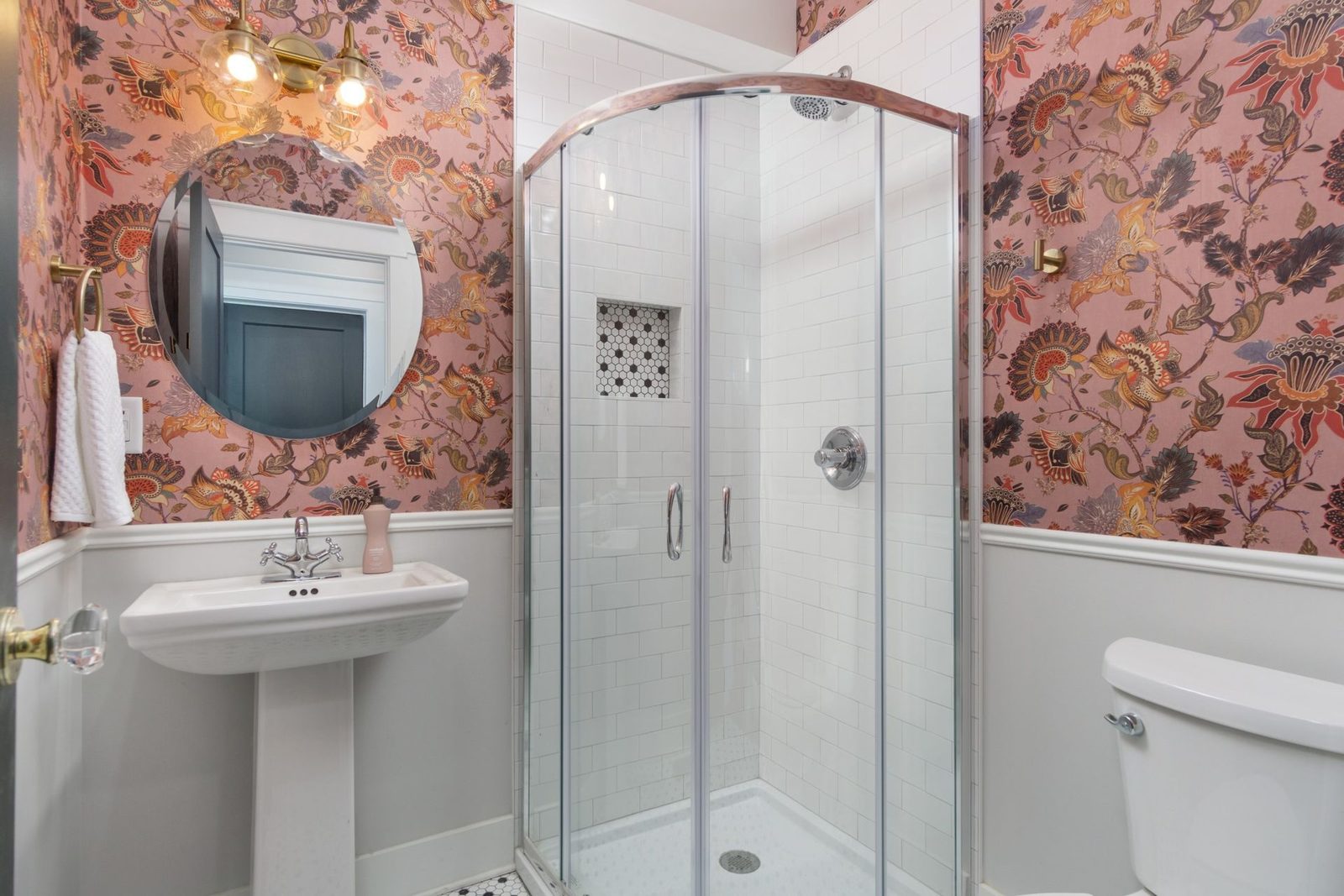 Bathroom with floral wallpaper, a pedestal sink and a corner glass shower