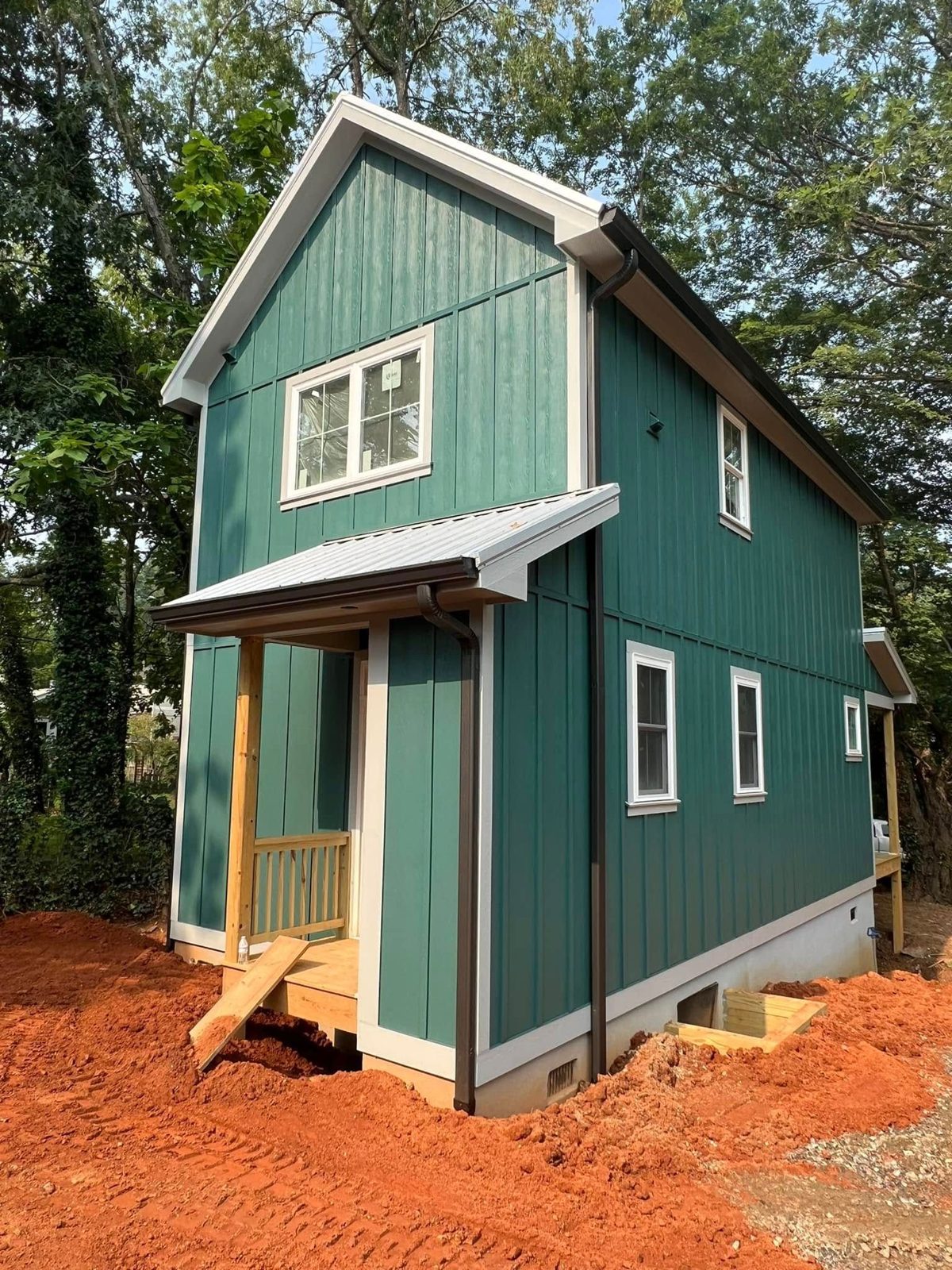 Teal board-and-batten new home with a covered entry, standing on freshly graded red clay