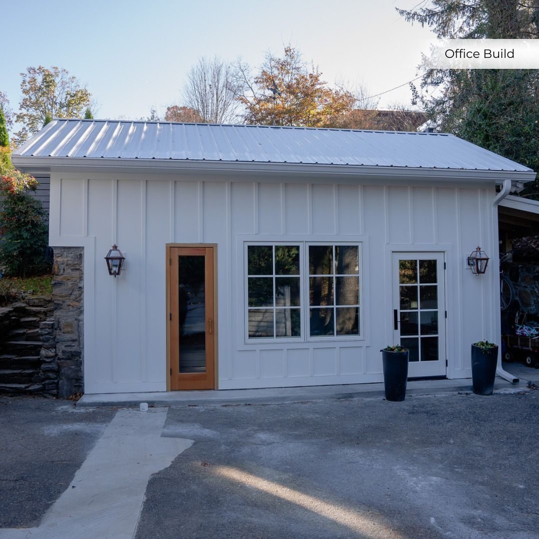 White board-and-batten office building with a wood door and lantern lights
